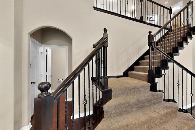 staircase with a high ceiling, arched walkways, and baseboards