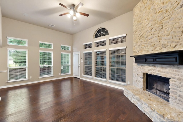 unfurnished living room featuring a ceiling fan, wood finished floors, a fireplace, baseboards, and a towering ceiling