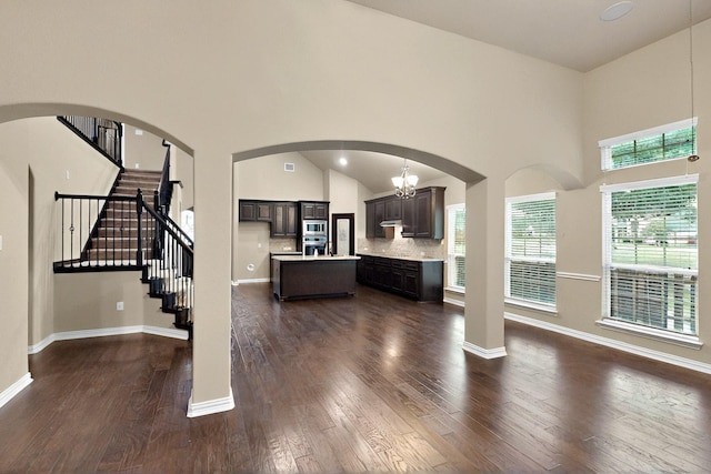 living area with dark wood finished floors, a towering ceiling, stairs, arched walkways, and baseboards