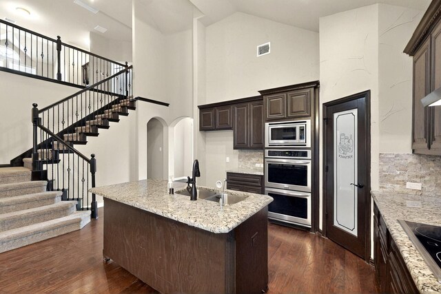 kitchen featuring stainless steel appliances, a sink, high vaulted ceiling, dark wood-type flooring, and tasteful backsplash