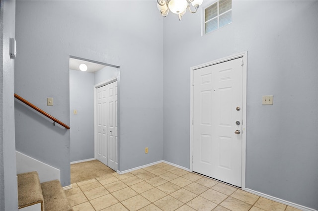 entryway featuring a towering ceiling, stairs, a chandelier, baseboards, and light tile patterned floors