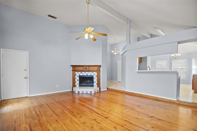 unfurnished living room featuring a chandelier, ceiling fan, a tile fireplace, light wood-style flooring, and beam ceiling