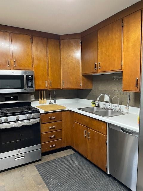 kitchen featuring stainless steel appliances, a sink, light countertops, and brown cabinets