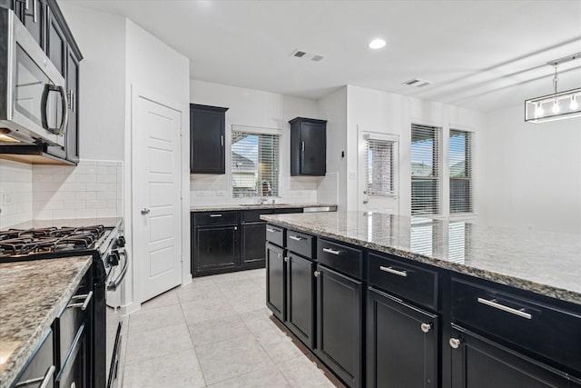 1706 Long Meadow Rd, Wylie, TX 75098 - kitchen with stainless steel microwave, dark cabinetry, range with gas stovetop, a sink, and decorative backsplash