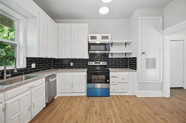 kitchen with stainless steel appliances, a sink, light wood finished floors, white cabinetry, and decorative backsplash