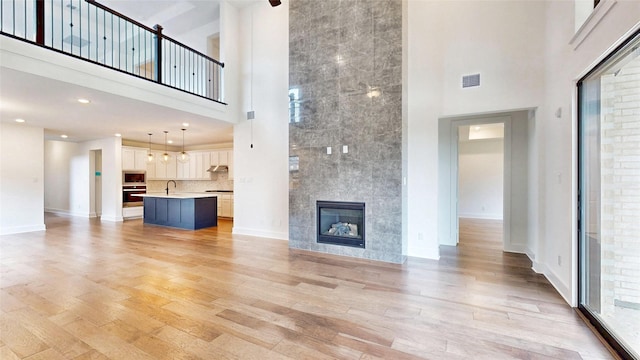 unfurnished living room featuring a towering ceiling, light wood-style flooring, a sink, baseboards, and a tile fireplace