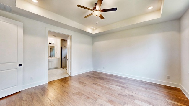 spare room with a raised ceiling, ceiling fan, light wood-type flooring, baseboards, and recessed lighting