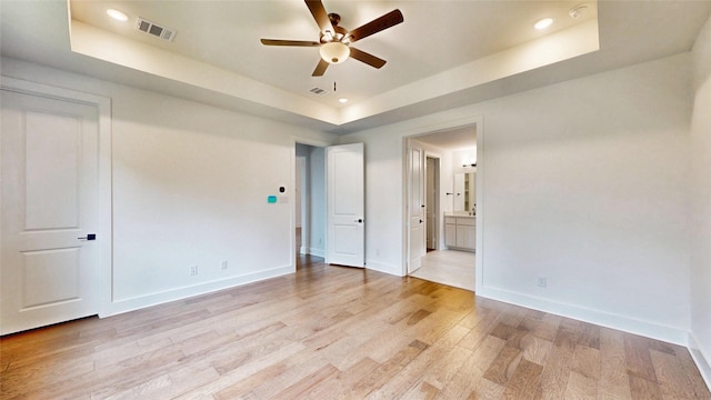 unfurnished bedroom with a raised ceiling, light wood finished floors, baseboards, ensuite bath, and recessed lighting