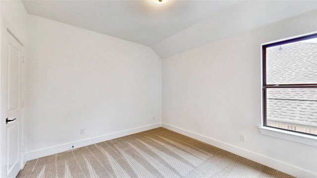 carpeted spare room featuring baseboards and vaulted ceiling