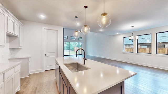 kitchen with a sink, light wood-type flooring, light countertops, white cabinetry, and baseboards