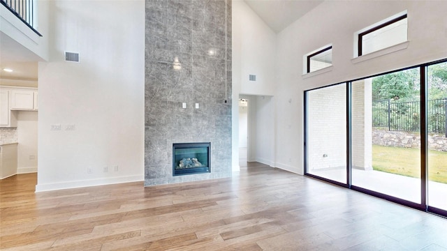 unfurnished living room with high vaulted ceiling, light wood finished floors, a fireplace, and baseboards