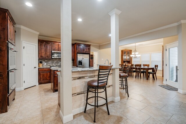 2687 Mcclendon Rd, Weatherford, TX 76088 - kitchen featuring appliances with stainless steel finishes, crown molding, a breakfast bar area, backsplash, and light stone countertops
