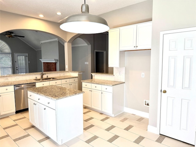 kitchen with dishwasher, a ceiling fan, a sink, arched walkways, and a kitchen island