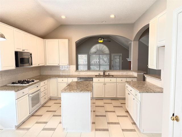 kitchen featuring white appliances, a sink, arched walkways, vaulted ceiling, and a center island