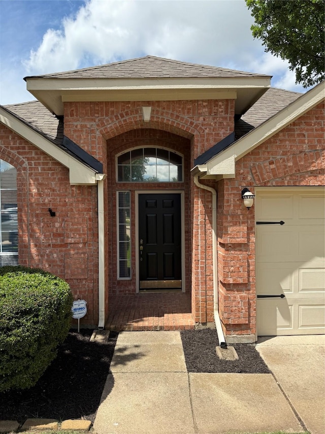 view of exterior entry featuring brick siding, roof with shingles, and a garage