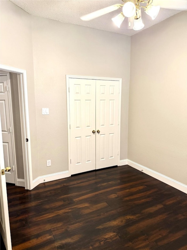 unfurnished bedroom with baseboards, dark wood-style flooring, a ceiling fan, and a closet