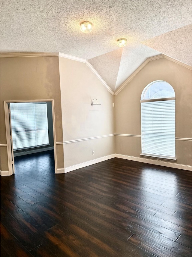 empty room with a textured ceiling, hardwood / wood-style floors, vaulted ceiling, and baseboards