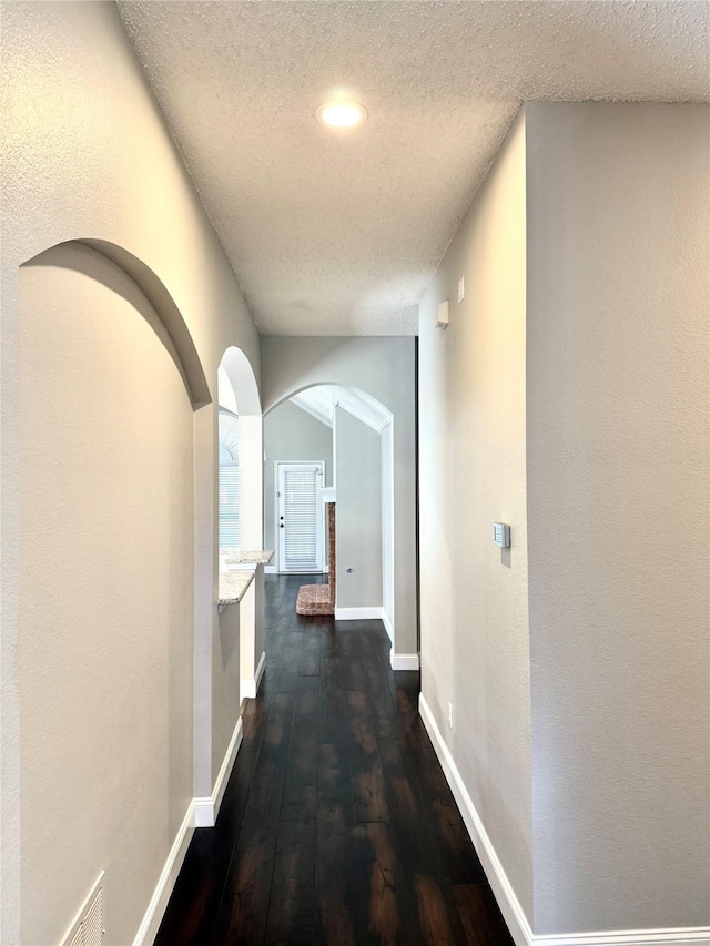 hallway featuring arched walkways, dark wood-style flooring, a textured ceiling, baseboards, and recessed lighting