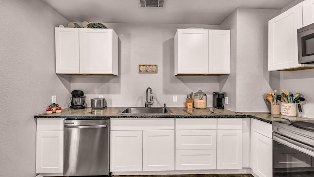 kitchen featuring stainless steel appliances, a sink, white cabinets, and a textured wall