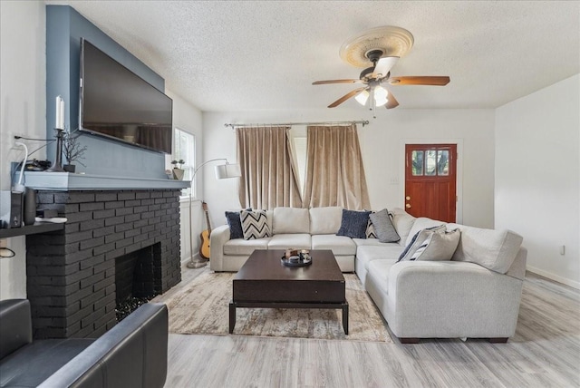 living room with a ceiling fan, wood finished floors, a textured ceiling, a brick fireplace, and baseboards