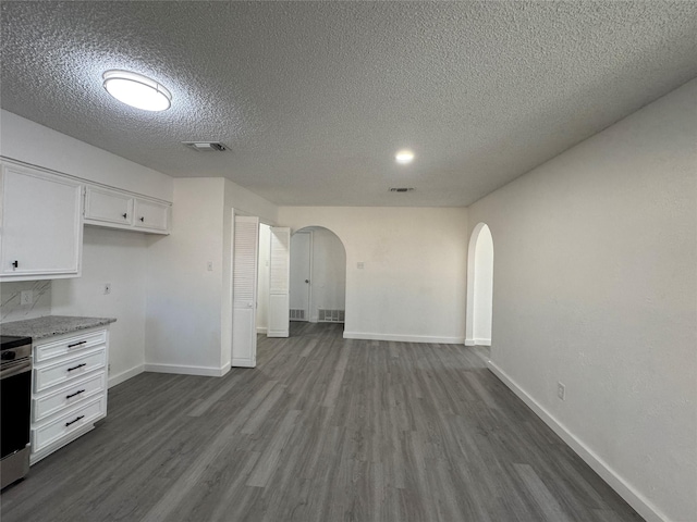 1029 Fox River Ln, Fort Worth, TX 76120 - kitchen with arched walkways, a textured ceiling, dark wood-style flooring, white cabinets, and baseboards