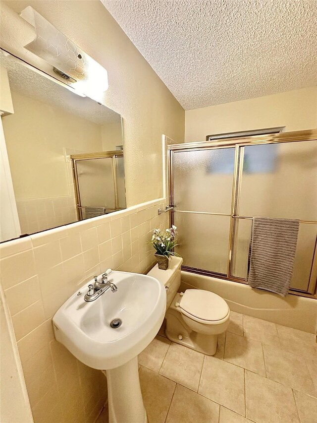 1008 Sierra Dr, Denton, TX 76209 - bathroom featuring a textured ceiling, tile walls, toilet, shower / bath combination with glass door, and tile patterned flooring