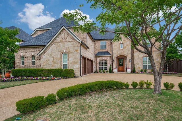 french country inspired facade featuring roof with shingles, concrete driveway, stone siding, and fence