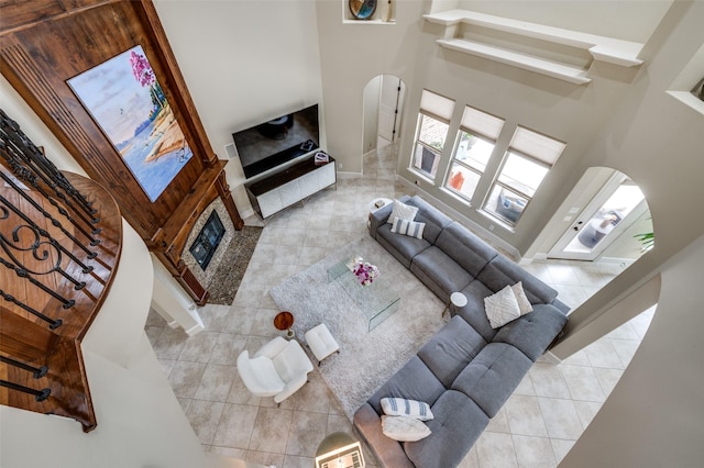 living room featuring arched walkways, a glass covered fireplace, tile patterned floors, a towering ceiling, and baseboards