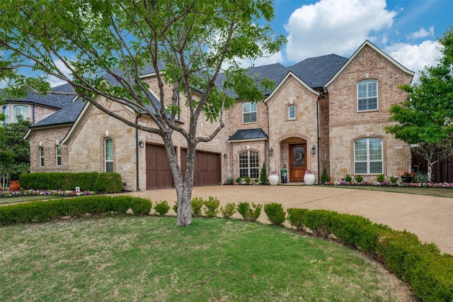 french country inspired facade featuring stone siding, concrete driveway, and a front yard
