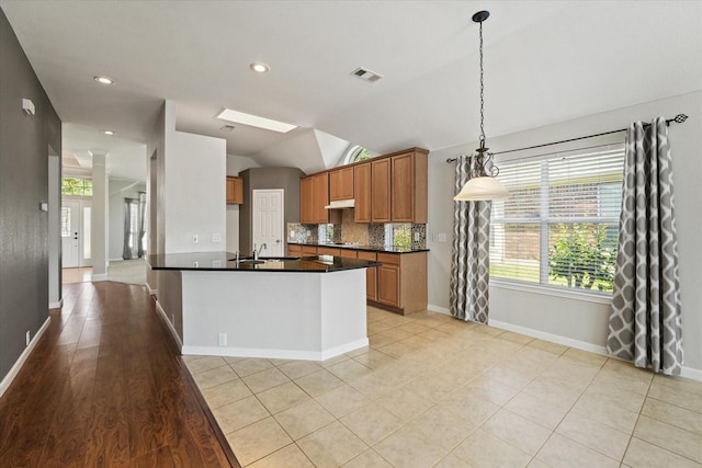 kitchen with dark countertops, a sink, vaulted ceiling, tasteful backsplash, and brown cabinetry