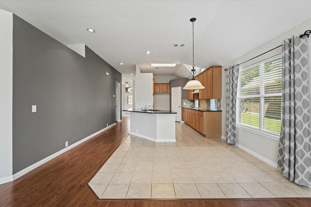 kitchen with dark countertops, brown cabinets, baseboards, open floor plan, and decorative backsplash