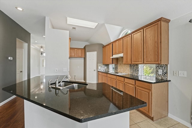 kitchen featuring a sink, under cabinet range hood, white stovetop, baseboards, and backsplash
