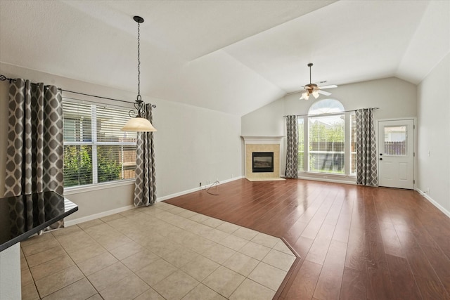 unfurnished living room with ceiling fan, healthy amount of natural light, vaulted ceiling, a fireplace, and baseboards