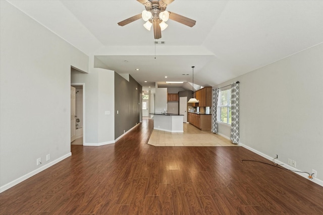 unfurnished living room with ceiling fan, baseboards, light wood-style flooring, and vaulted ceiling