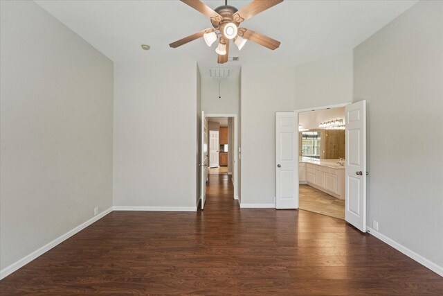 unfurnished bedroom with attic access, wood finished floors, baseboards, ensuite bath, and a towering ceiling