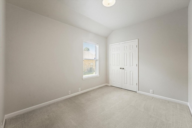 unfurnished bedroom with light carpet, baseboards, vaulted ceiling, and a closet