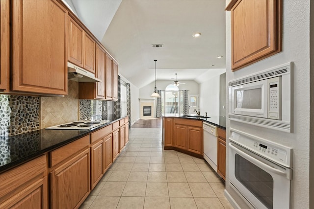 kitchen featuring white appliances, under cabinet range hood, a sink, vaulted ceiling, and backsplash
