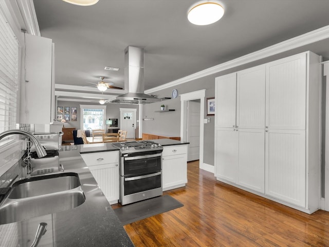 1942 Fairmount Ave, Fort Worth, TX 76110 - kitchen featuring range with two ovens, a sink, island exhaust hood, dark countertops, and white cabinetry