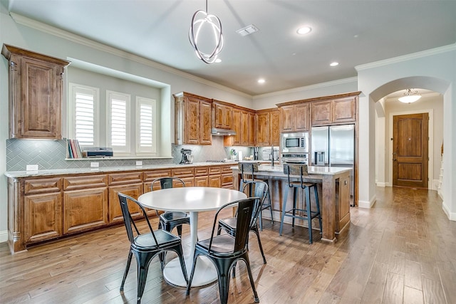 4701 Trevor Trl, Grapevine, TX 76051 - kitchen with stainless steel appliances, under cabinet range hood, arched walkways, a kitchen island, and brown cabinets