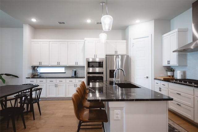 kitchen featuring appliances with stainless steel finishes, a sink, wall chimney range hood, tasteful backsplash, and light wood-style floors