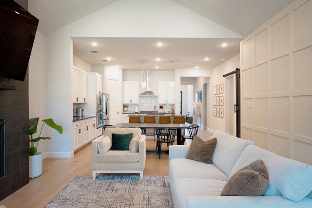 living area with a barn door, lofted ceiling, light wood-type flooring, recessed lighting, and baseboards