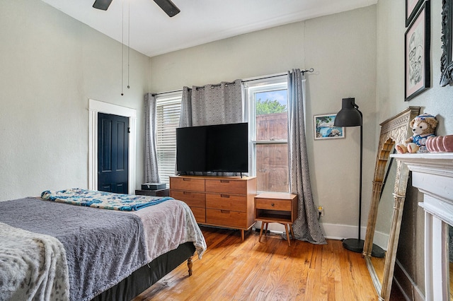 bedroom with wood finished floors, a ceiling fan, baseboards, and a fireplace