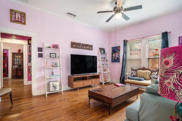 living area featuring a ceiling fan, wood finished floors, crown molding, and baseboards