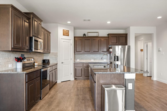kitchen with appliances with stainless steel finishes, a sink, light wood-type flooring, stone countertops, and recessed lighting