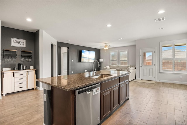 kitchen with a sink, dishwasher, light wood-style floors, dark brown cabinetry, and dark stone countertops