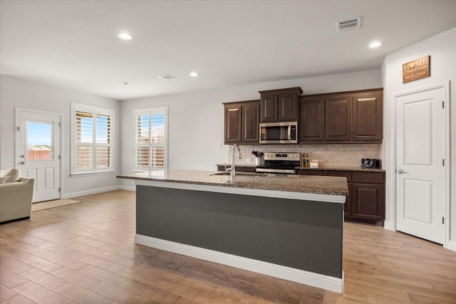 kitchen with stainless steel appliances, decorative backsplash, a sink, light wood-style flooring, and dark brown cabinets