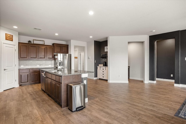 kitchen featuring appliances with stainless steel finishes, a sink, an island with sink, light wood-style flooring, and recessed lighting