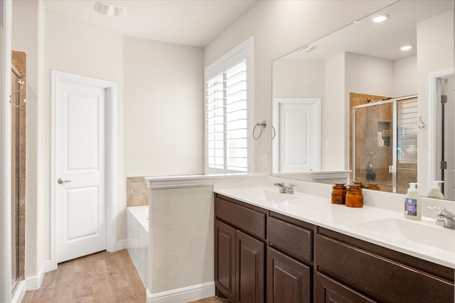 bathroom with a shower stall, a garden tub, double vanity, and wood finished floors