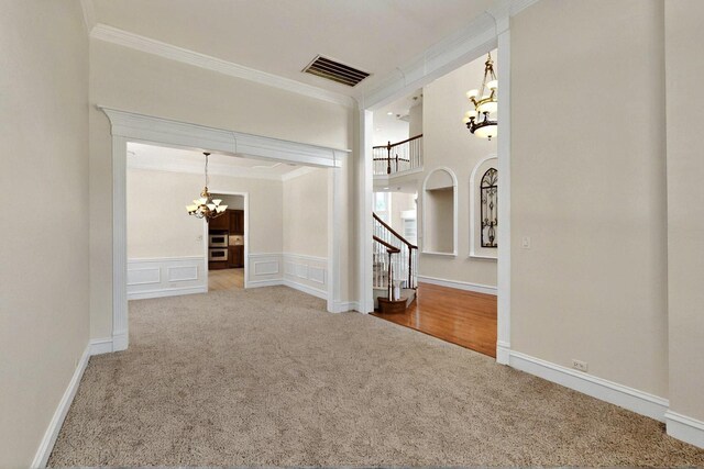 entryway with a chandelier, carpet, crown molding, stairs, and a wainscoted wall