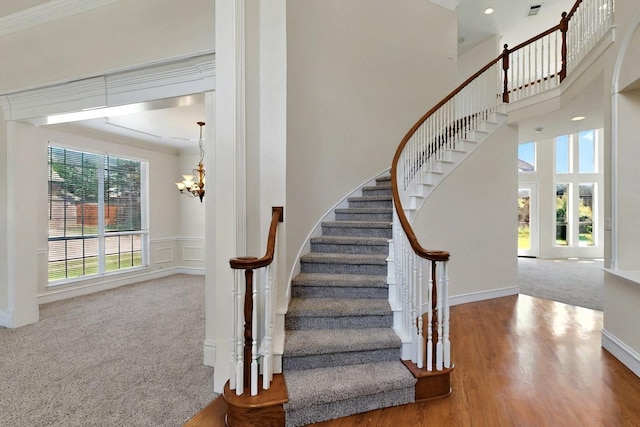 stairway featuring a chandelier, crown molding, carpet floors, a towering ceiling, and wood finished floors